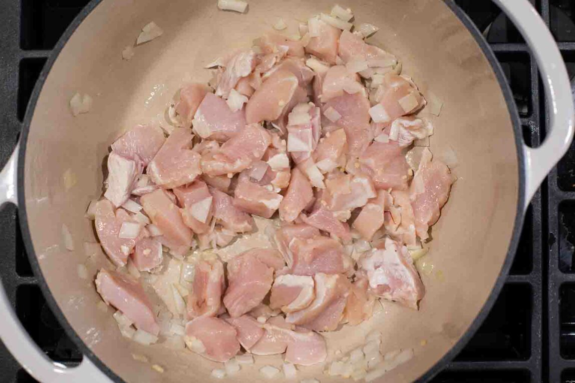 Raw chicken breast being cooked in a dutch oven.