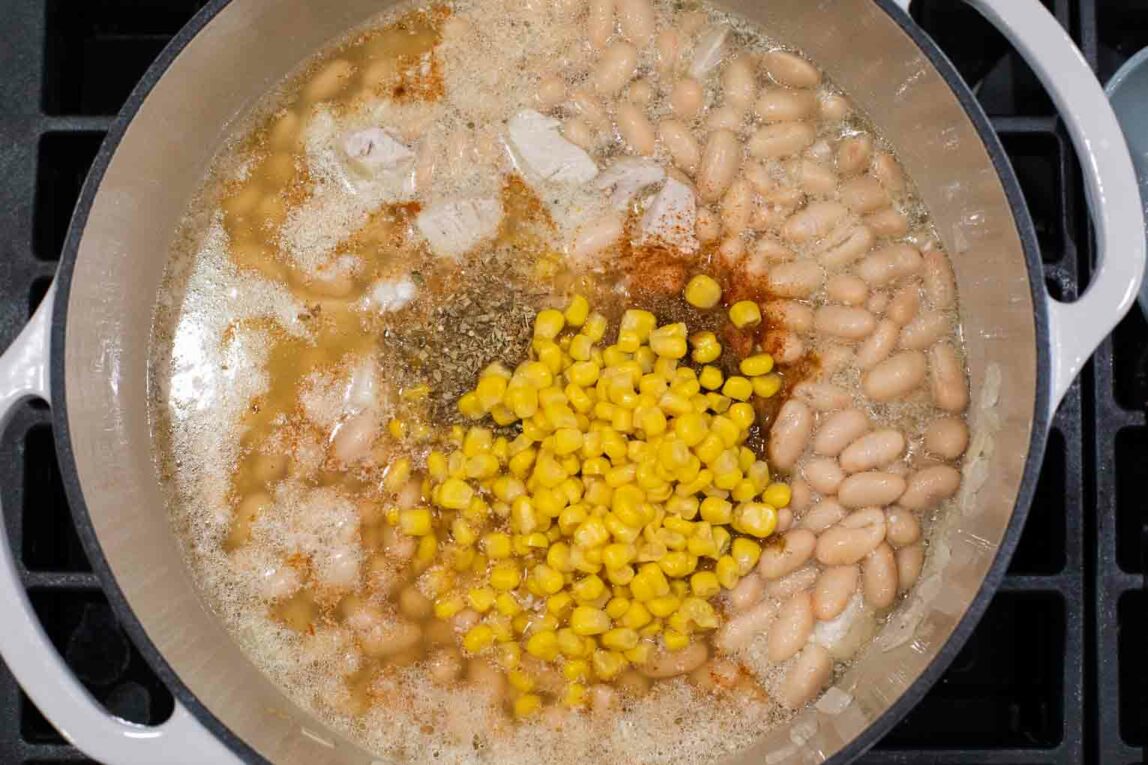 White beans, chili spices, and corn being cooked in a dutch oven.