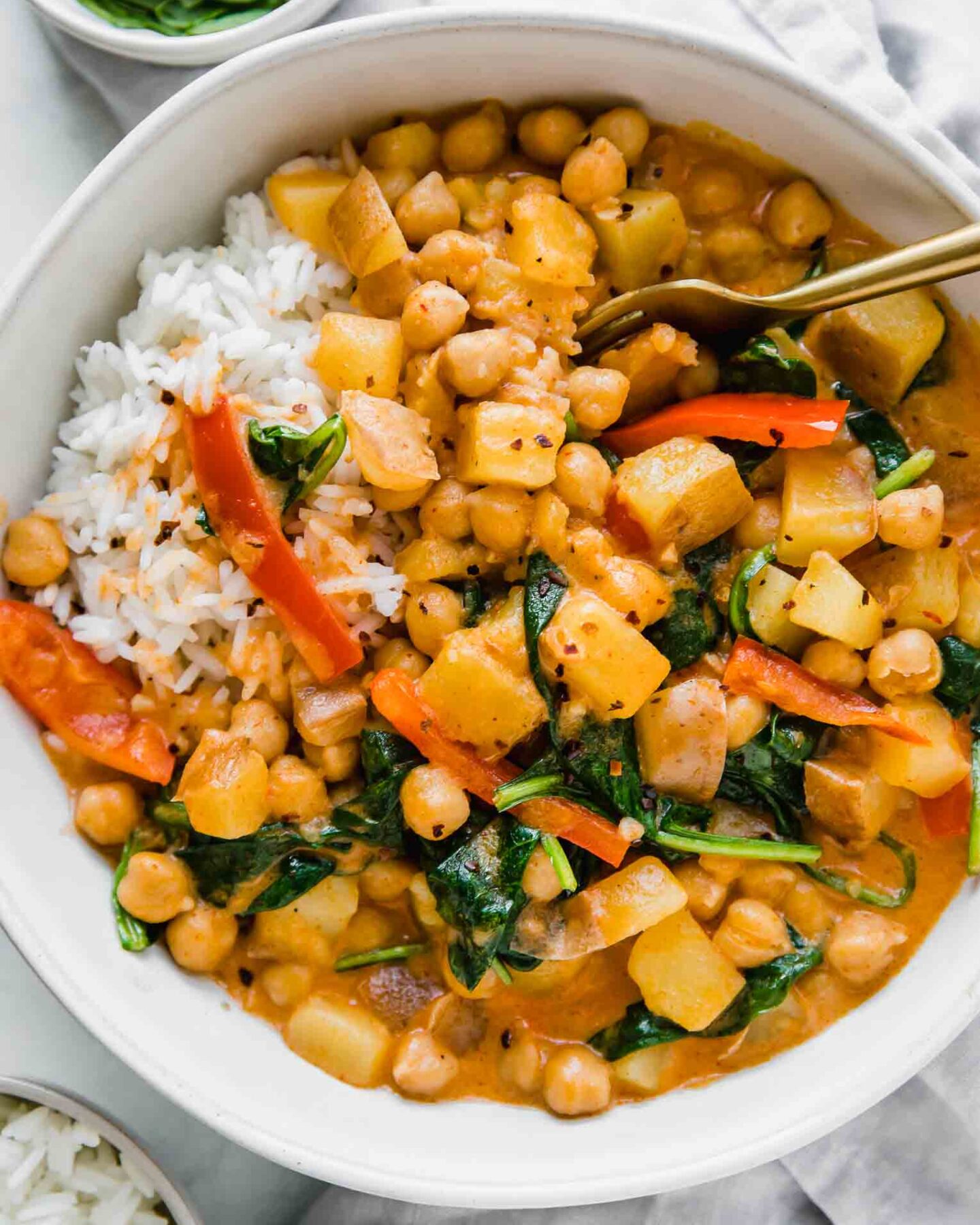 Easy Vegan Potato Curry in a white bowl next to spinach and rice.