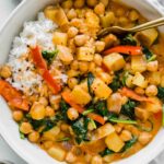 Easy Vegan Potato Curry in a white bowl next to spinach and rice.