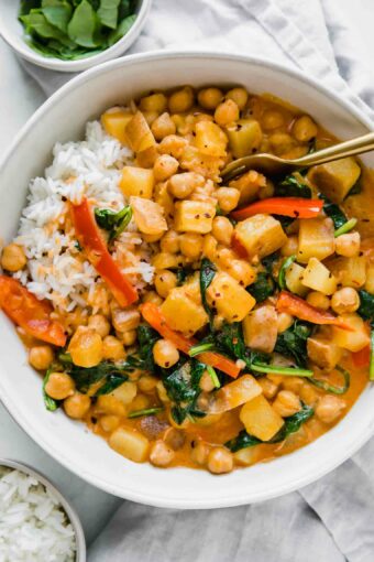 Easy Vegan Potato Curry in a white bowl next to spinach and rice.
