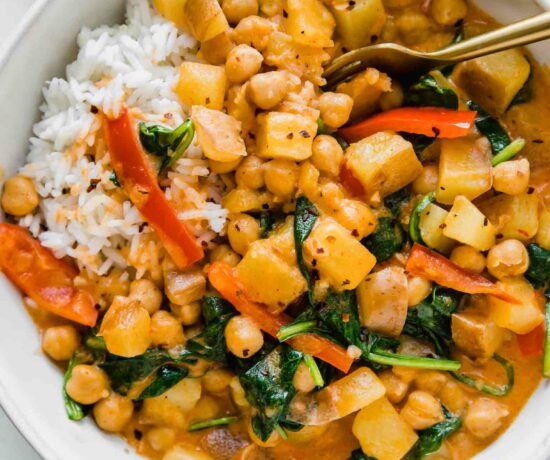 Easy Vegan Potato Curry in a white bowl next to spinach and rice.