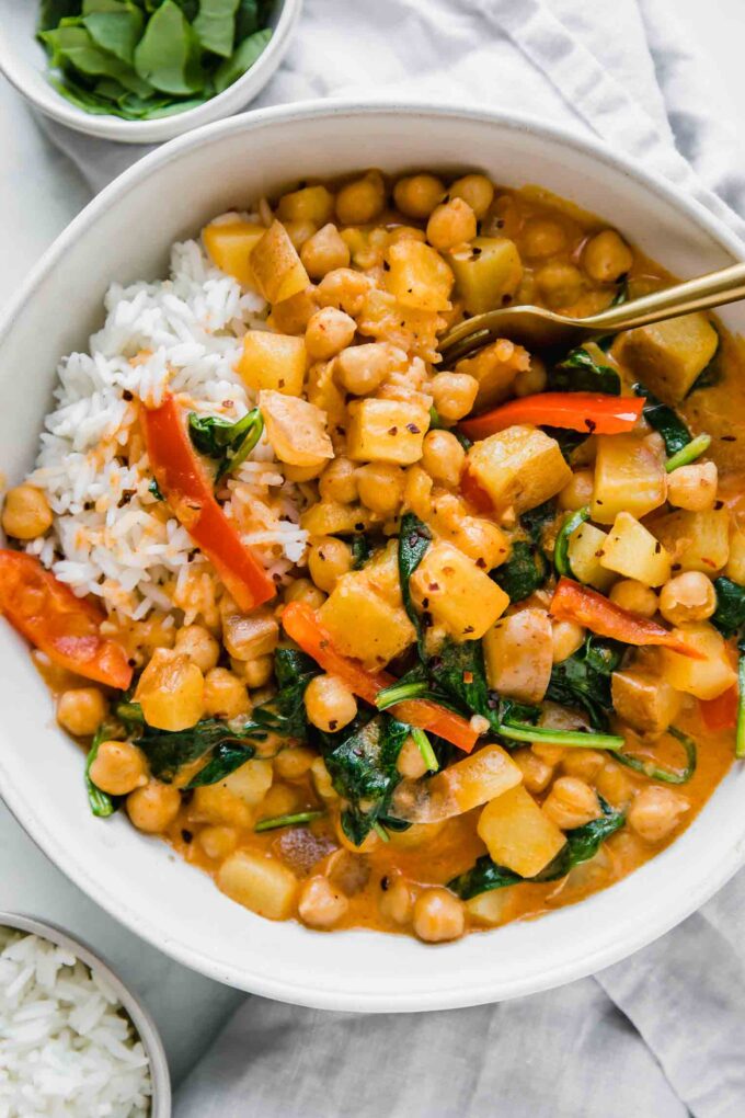 Easy Vegan Potato Curry in a white bowl next to spinach and rice.