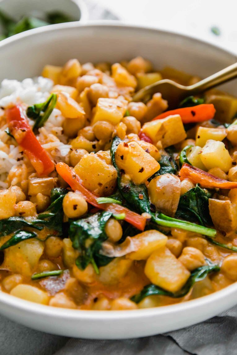 Angled close up of potatoes, peppers, kale, and chickpeas in a curry sauce.
