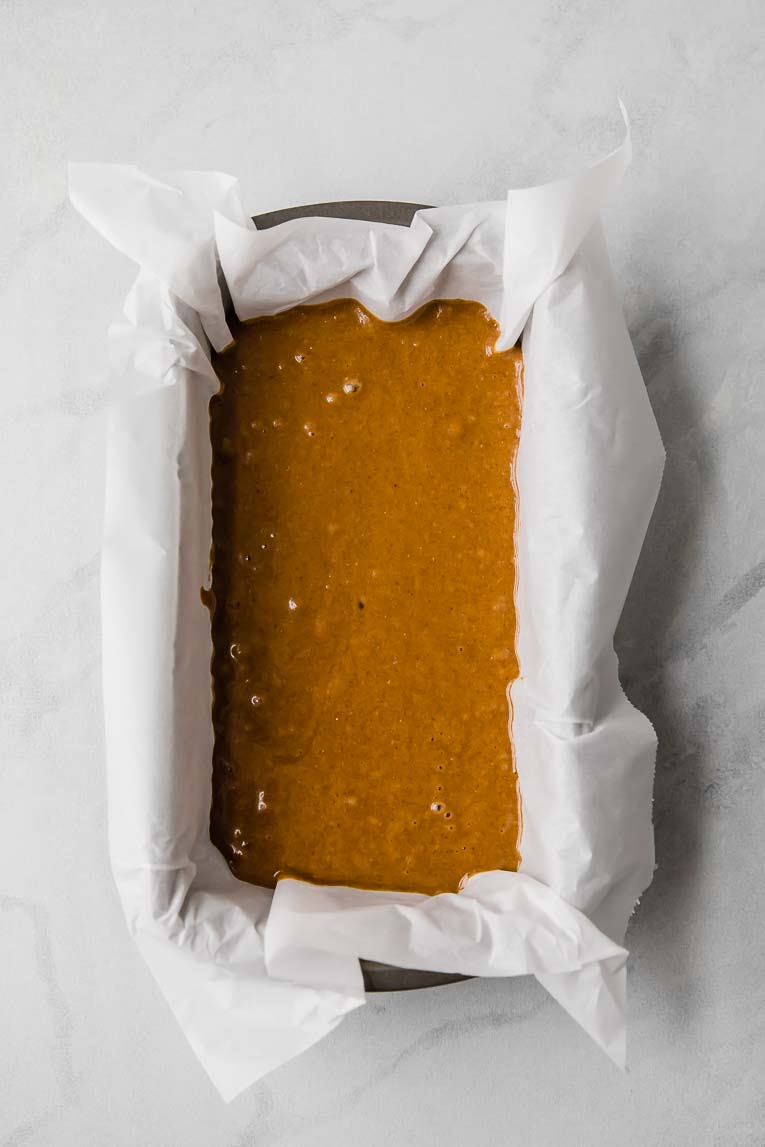 Gingerbread batter in a loaf pan lined with parchment paper.