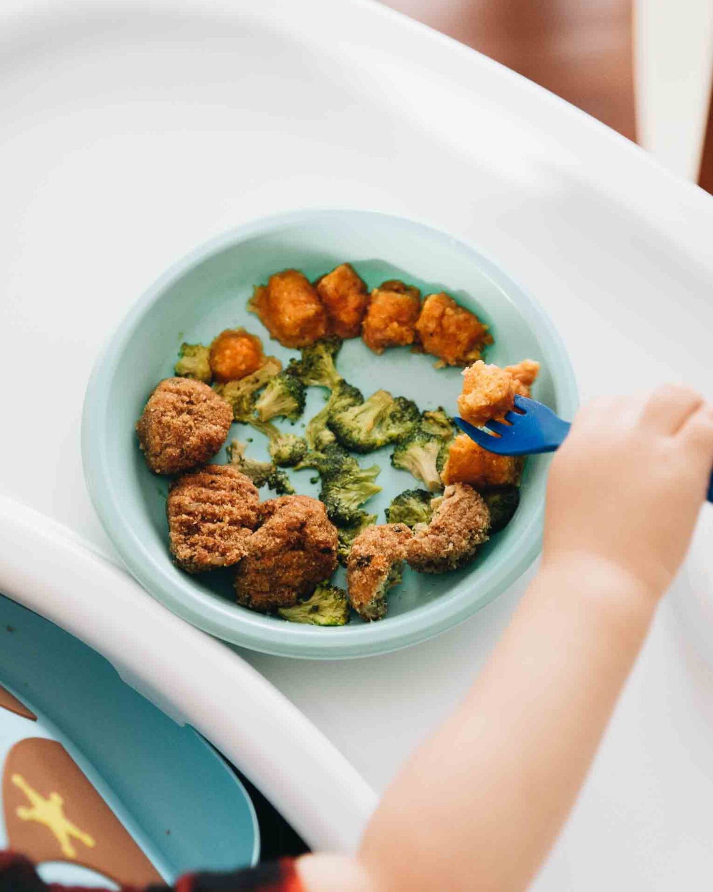 Toddler holding fork eating healthy meal.