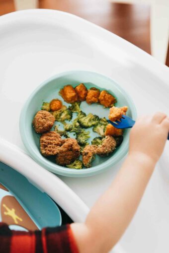 Toddler holding fork eating healthy meal.