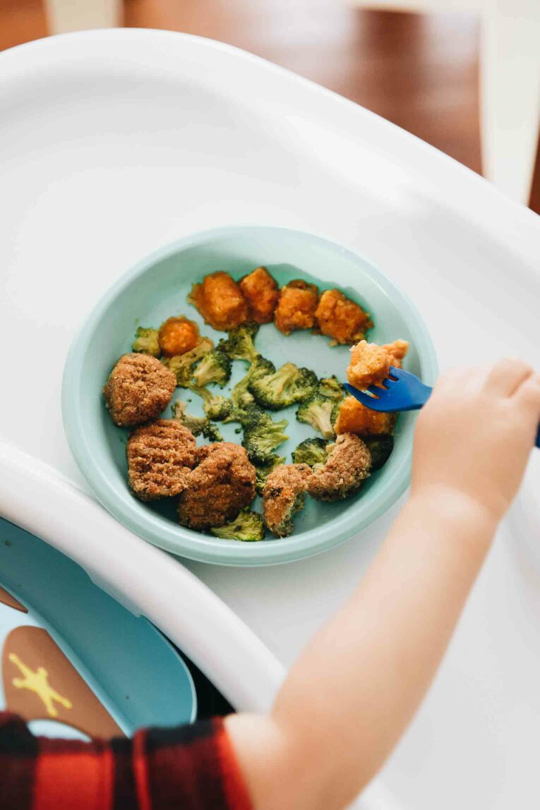 Toddler holding fork eating healthy meal.