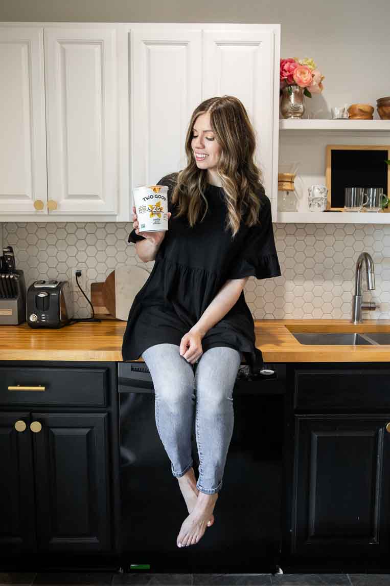 Girl holding Two Good Vanilla Greek Yogurt in hand in kitchen.