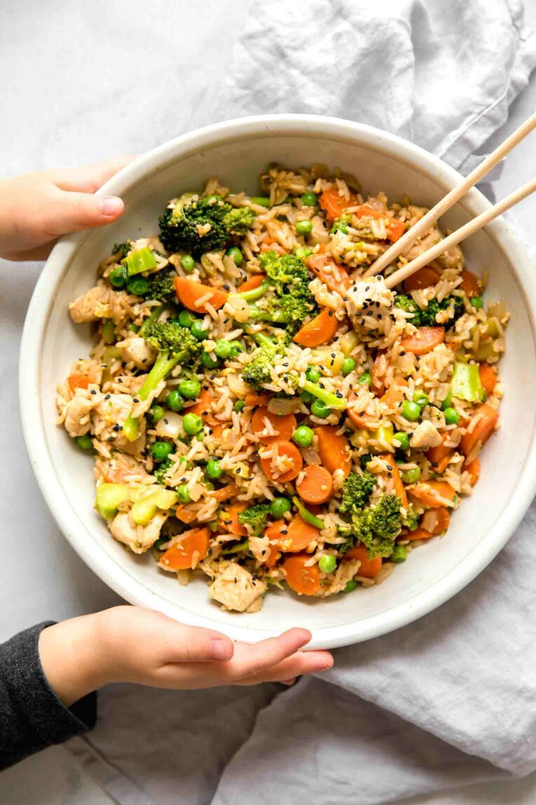 Toddler hands holding a bowl of chicken fried rice.