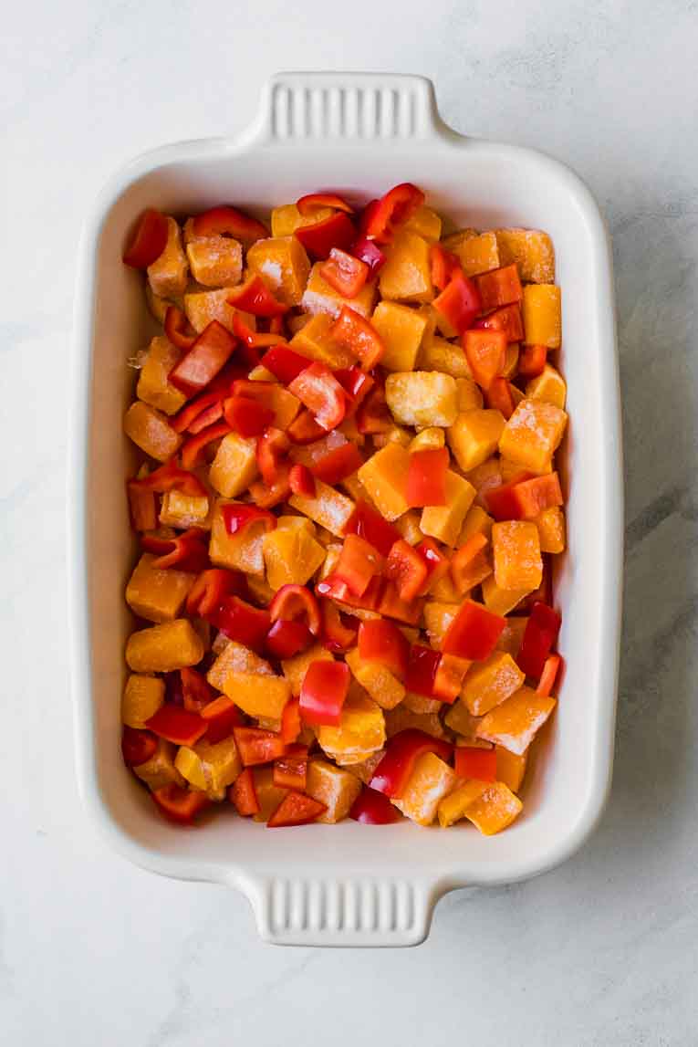 Chopped peppers and frozen butternut squash in a casserole dish.