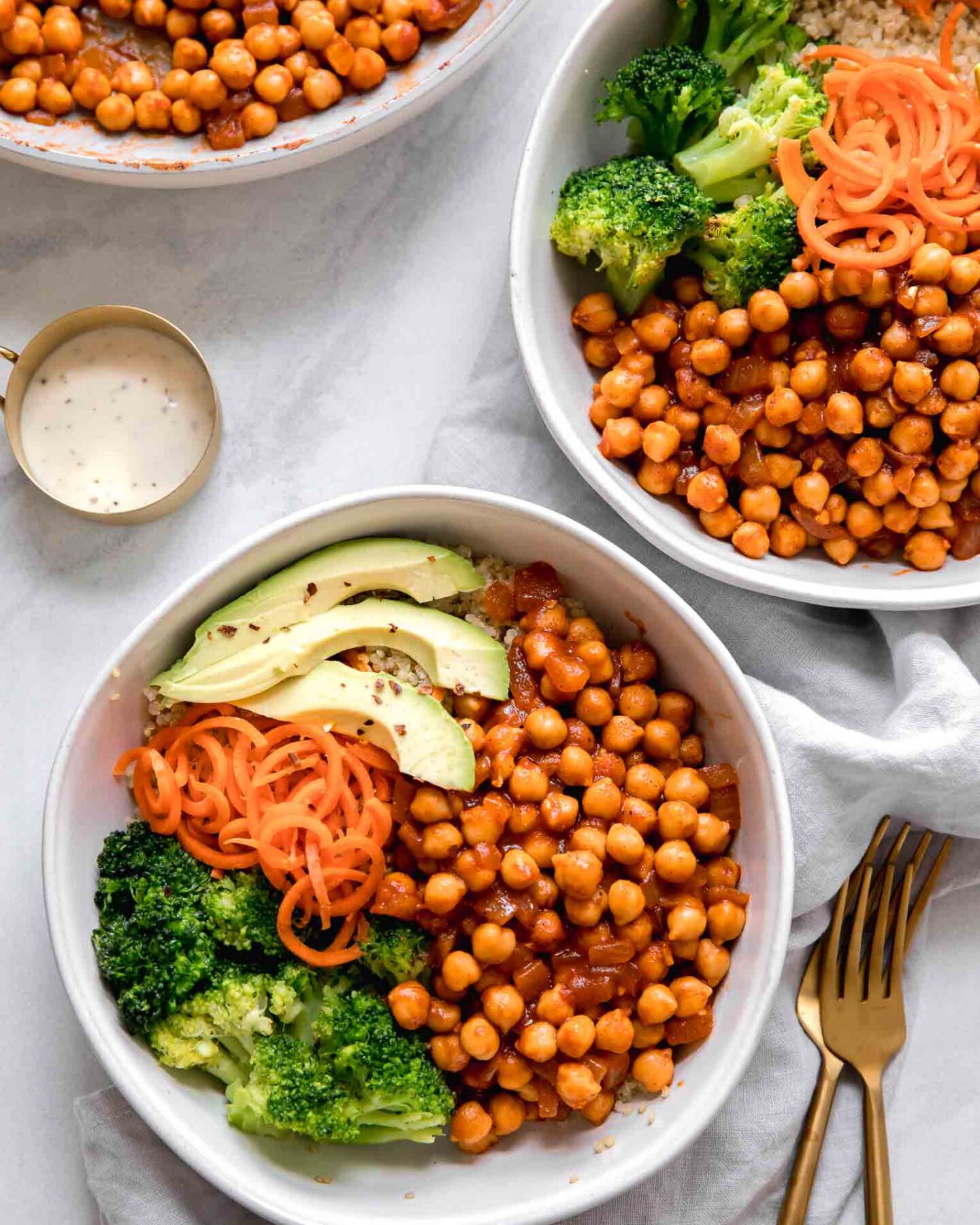 Two chickpea bowls with vegan buffalo sauce on a marble countertop.