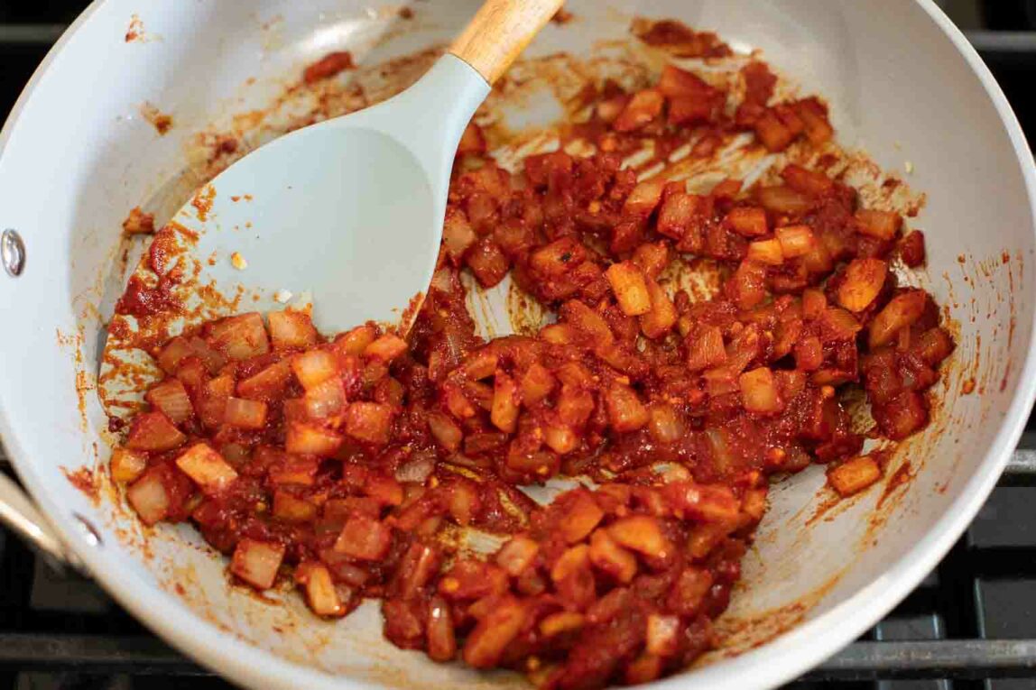 Onions, garlic, and tomato sauce being cooked in a pan.