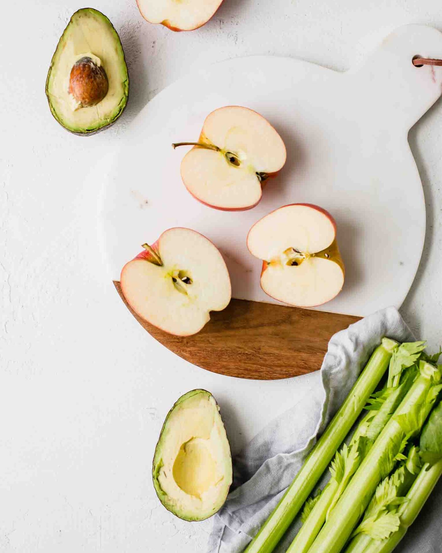 Sliced apples, avocado, and celery on a countertop.