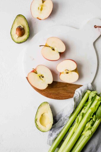 Sliced apples, avocado, and celery on a countertop.