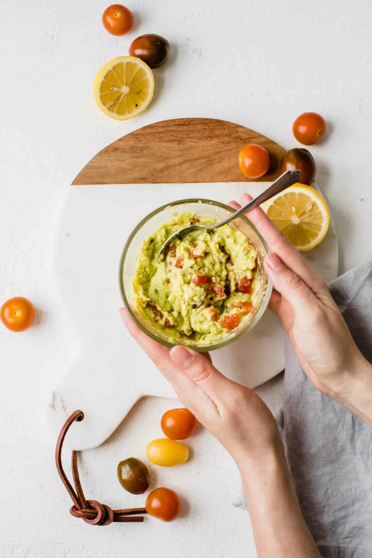 Hands holding bowl of guacamole.