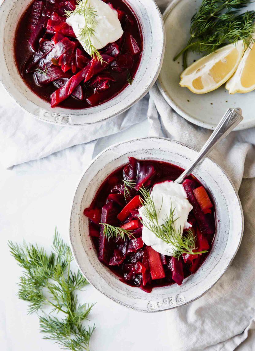 Two bowls of Borscht soup with a plate of lemon wedges on the side.