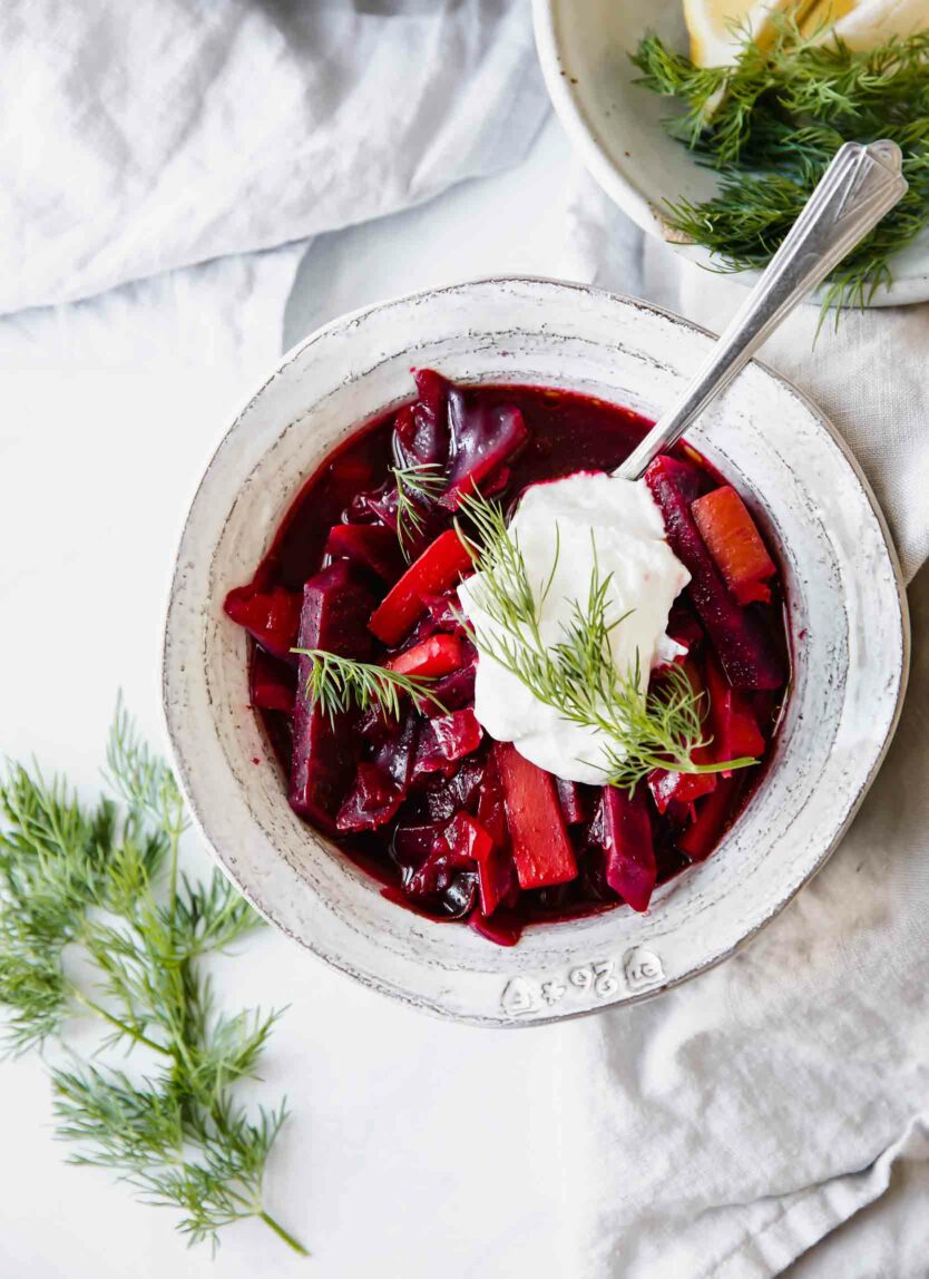 A single bowl of Borscht soup with a spoon and a scoop of yogurt over top.