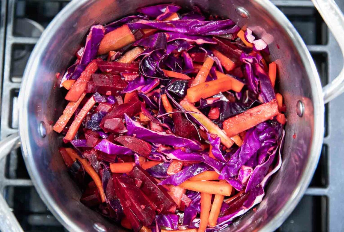 Carrots and beets being cooked in a pot over a stove.