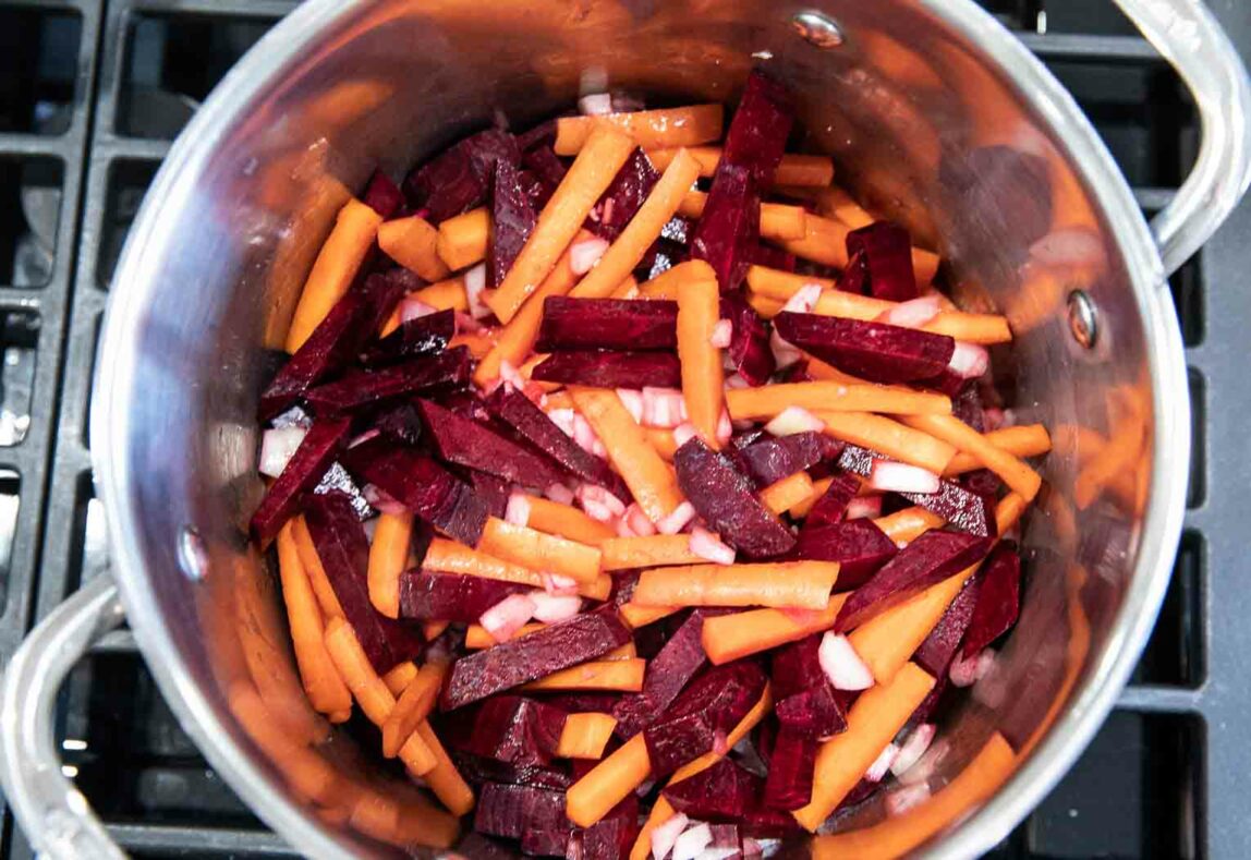 Sliced carrots and cabbage being cooked in a pot over a stove.