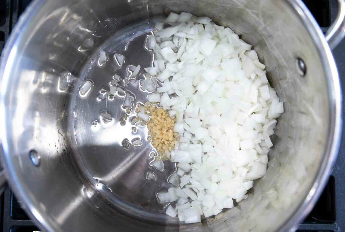 Chopped onions and garlic in a pot over a stove.