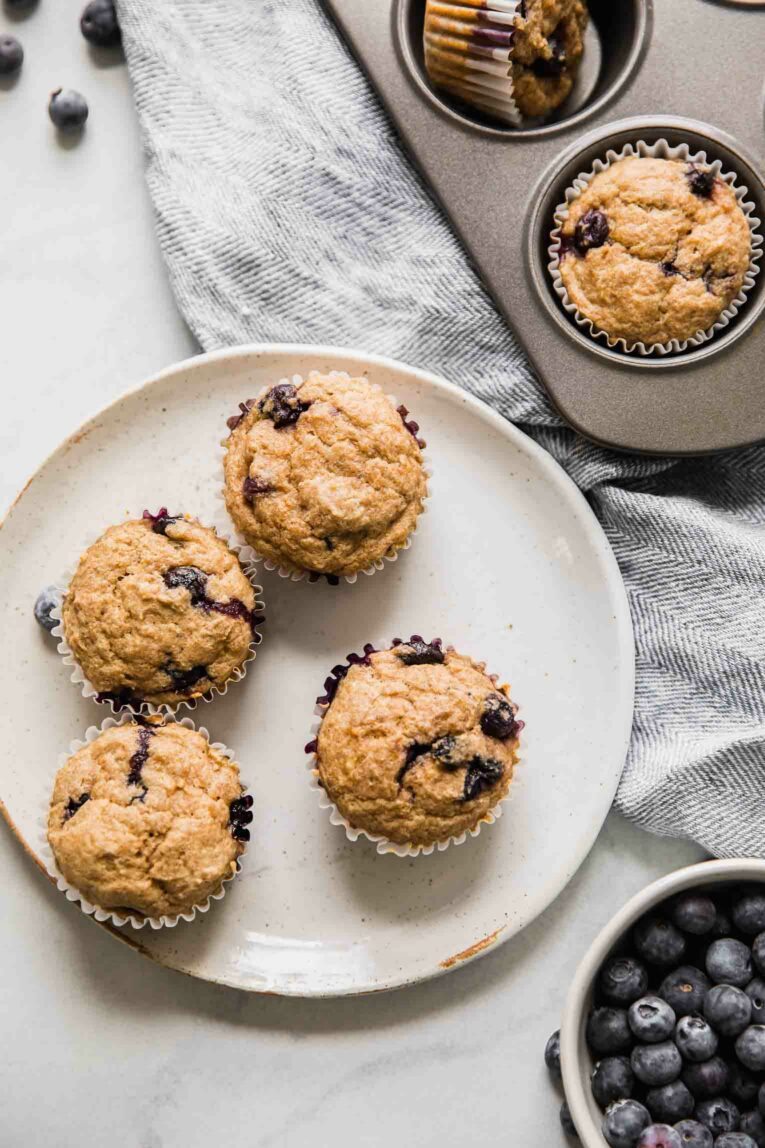 Toddler muffins on a white plate next to bowl of blueberries.