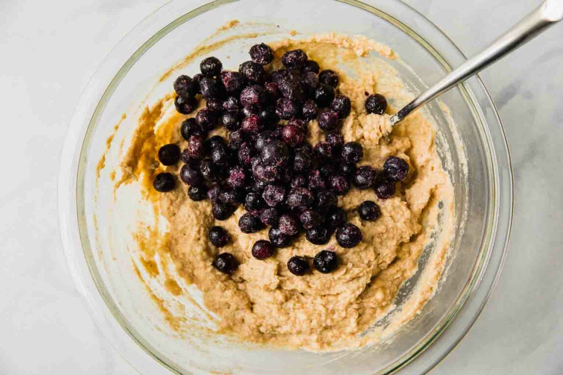 Toddler muffin batter with blueberries being mixed in a bowl.