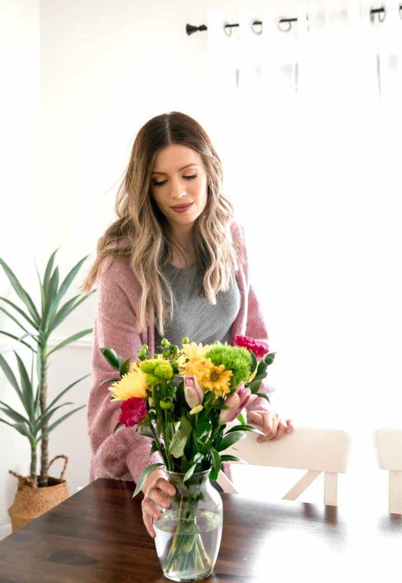 Woman is placing a vase of flowers on a table.