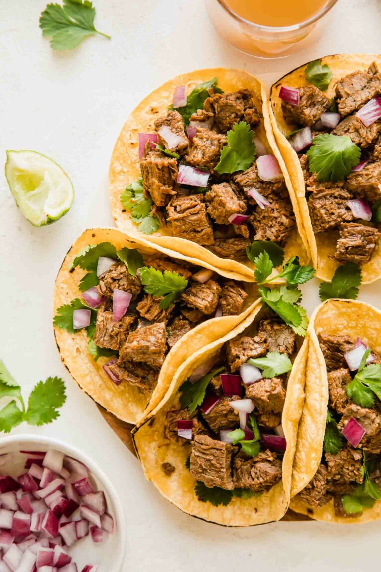 Instant Pot Carne Asada Tacos with a drink and bowl of chopped onions.