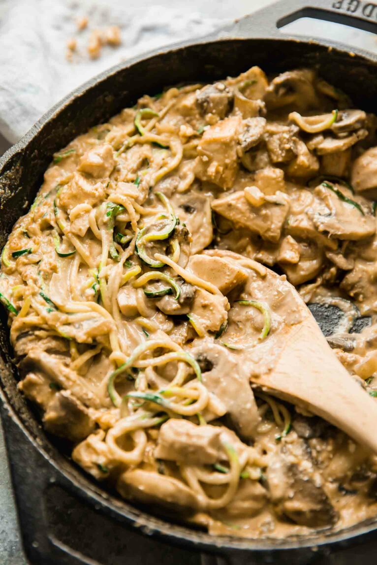 Chicken casserole that is paleo in a skillet with a wooden spoon.