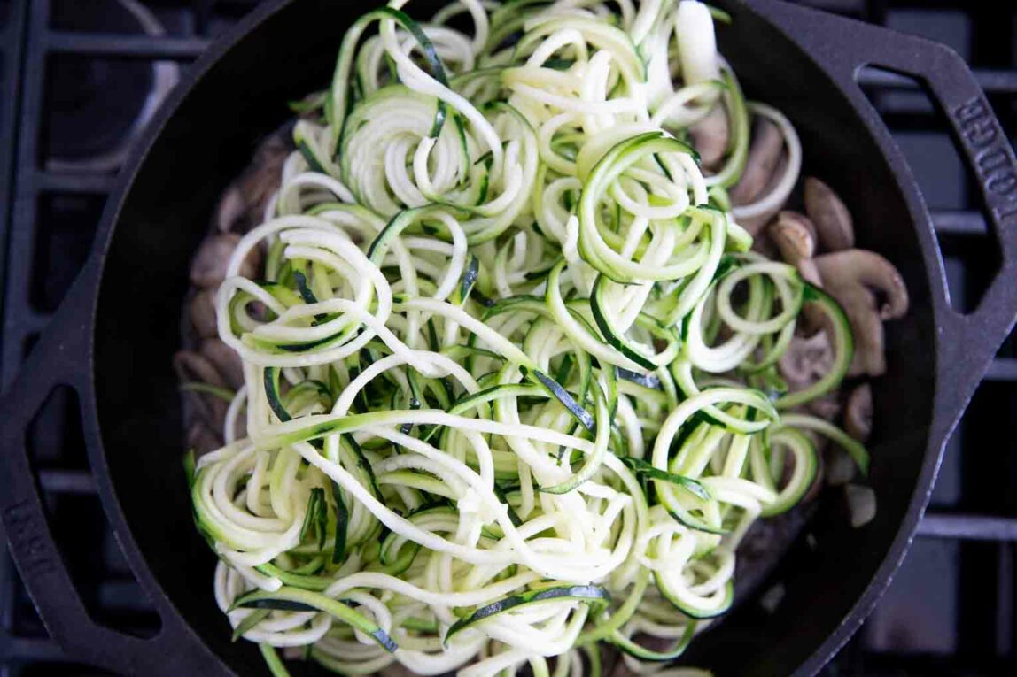 Zucchini spirals being sautéed in a skillet.