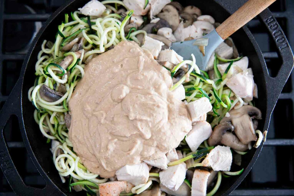 Zucchini spirals and cashew butter being sauteed in a skillet.