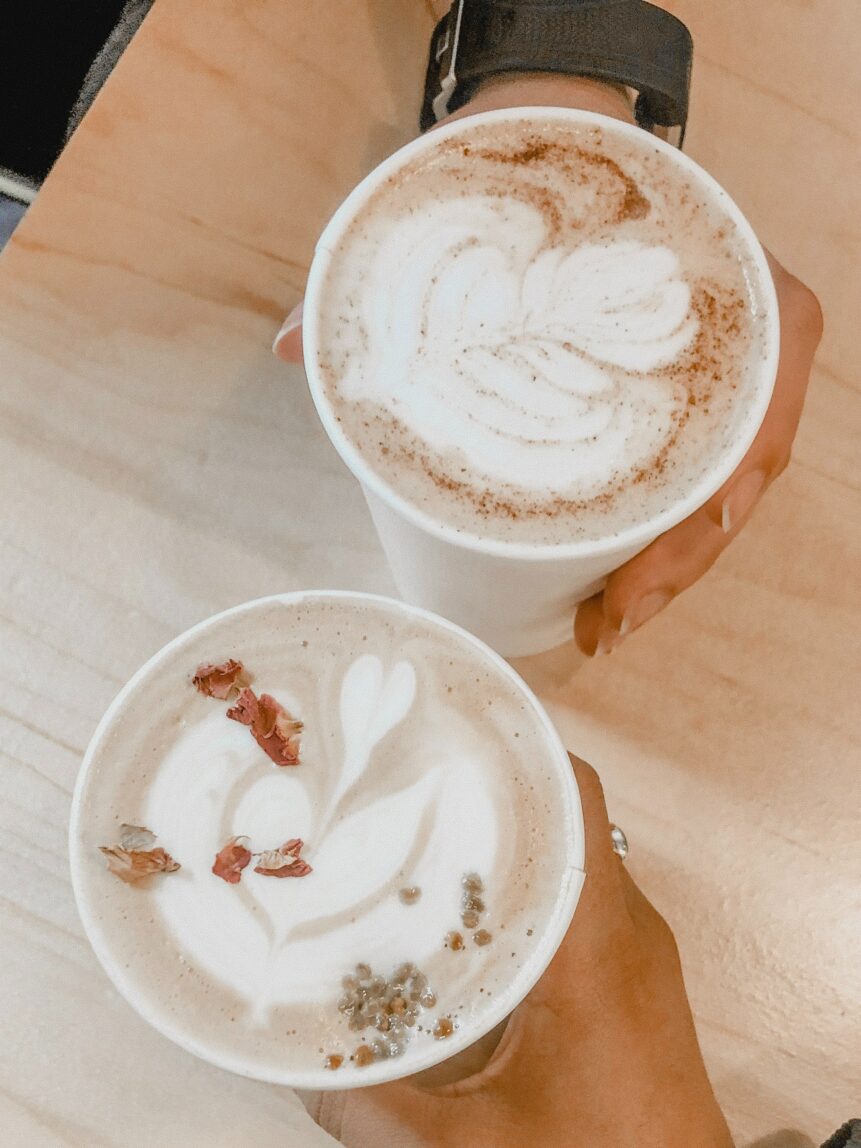 Two hands holding two latte art coffee beverages.