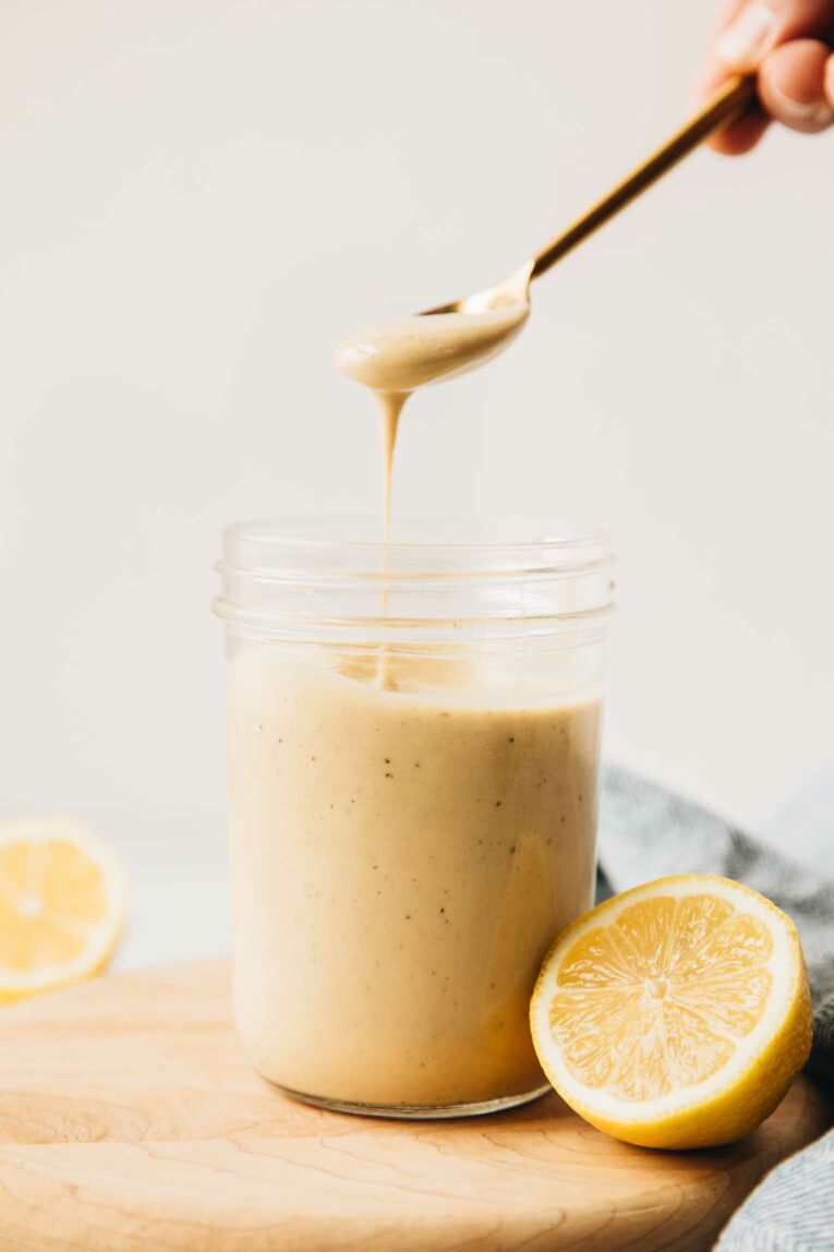 Mason jar of lemon tahini dressing with spoon coming out.