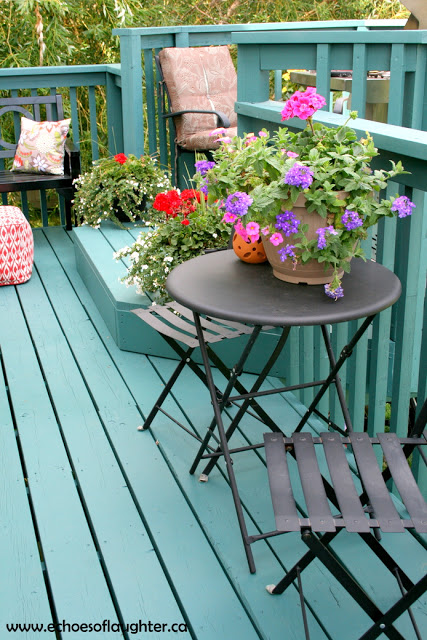 A turquoise painted deck with a table and flowers.