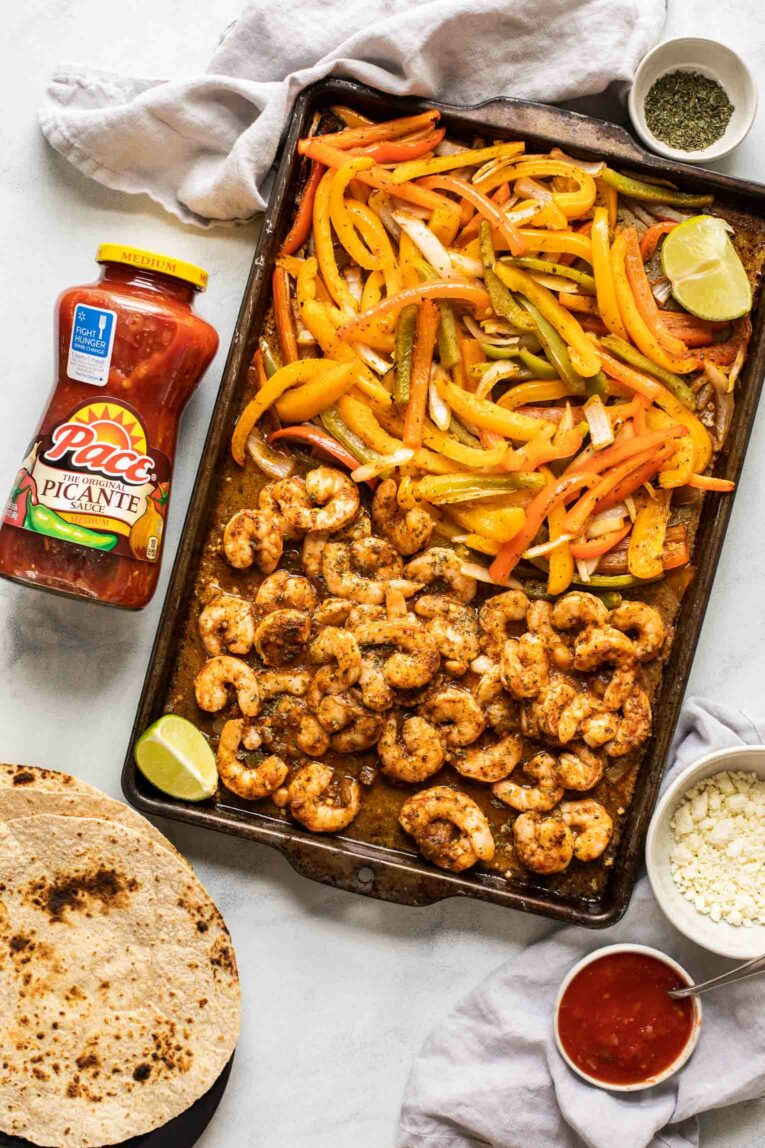 Sheet pan shrimp fajitas on a baking pan next to tortillas and Pace Picante Salsa.