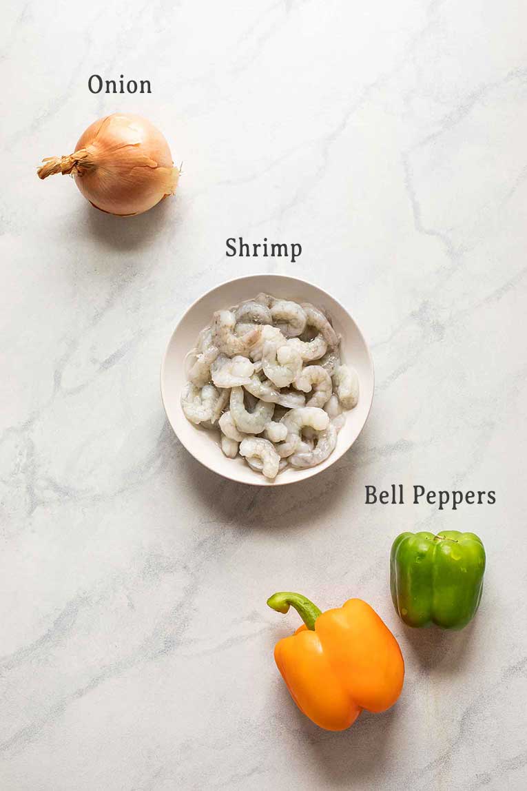 Shrimp, onion, and bell peppers on a marble board.