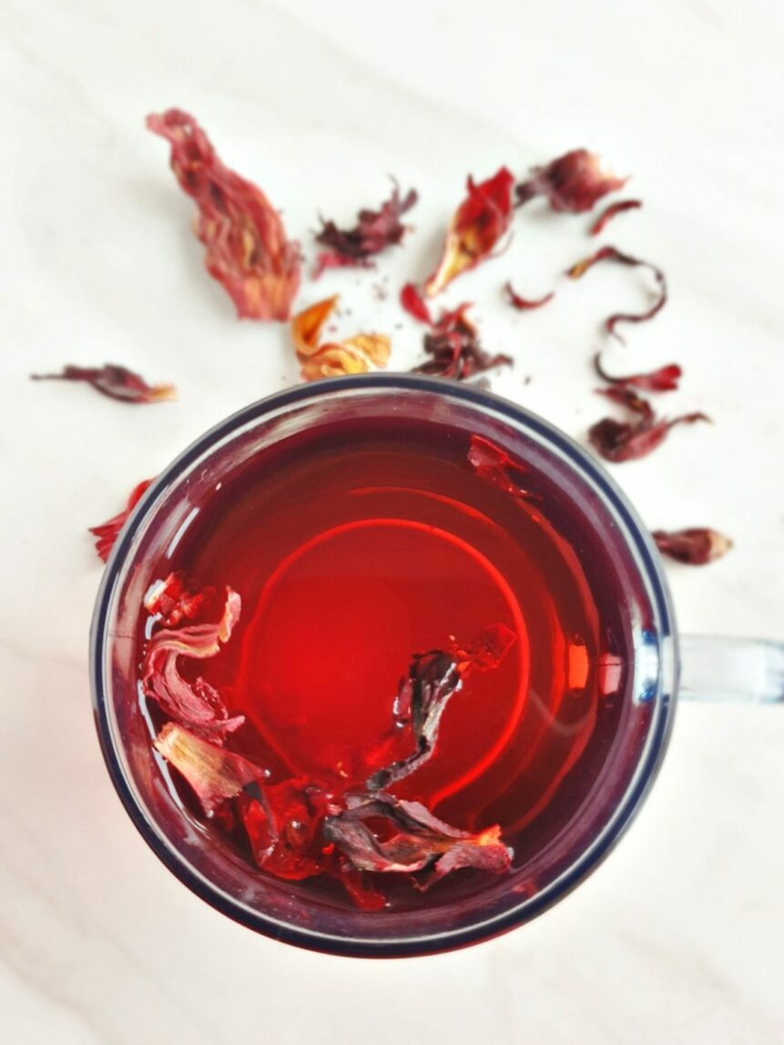 A mug of hibiscus tea with tea leaves around it. 