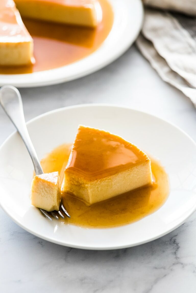 An image of a piece of flan cake on a plate with a fork next to it.
