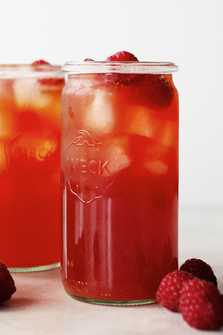 Two glass jars filled with raspberry iced tea and raspberries on the sides. 