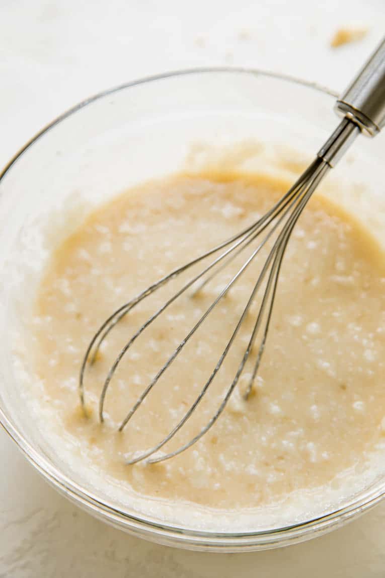 A glass mixing bowl of muffin mix with a whisk inside of the bowl.