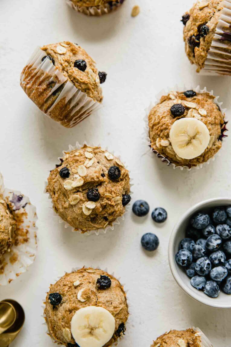 Several cooled muffins with banana toppings and a small bowl of blueberries on the side.
