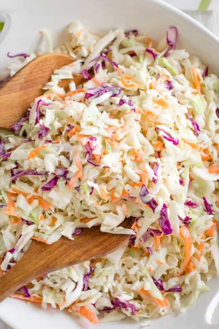 A top shot of a bowl of coleslaw with two wooden spoons. 