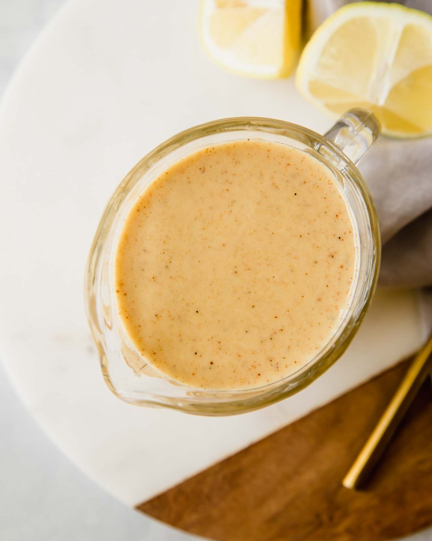 A top shot of a creamer filled with honey mustard on a wooden and ceramic cutting board.