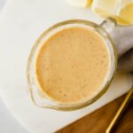 A top shot of a creamer filled with honey mustard on a wooden and ceramic cutting board.