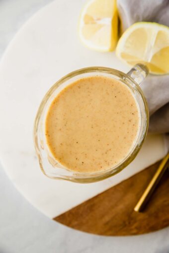 A top shot of a creamer filled with honey mustard on a wooden and ceramic cutting board.