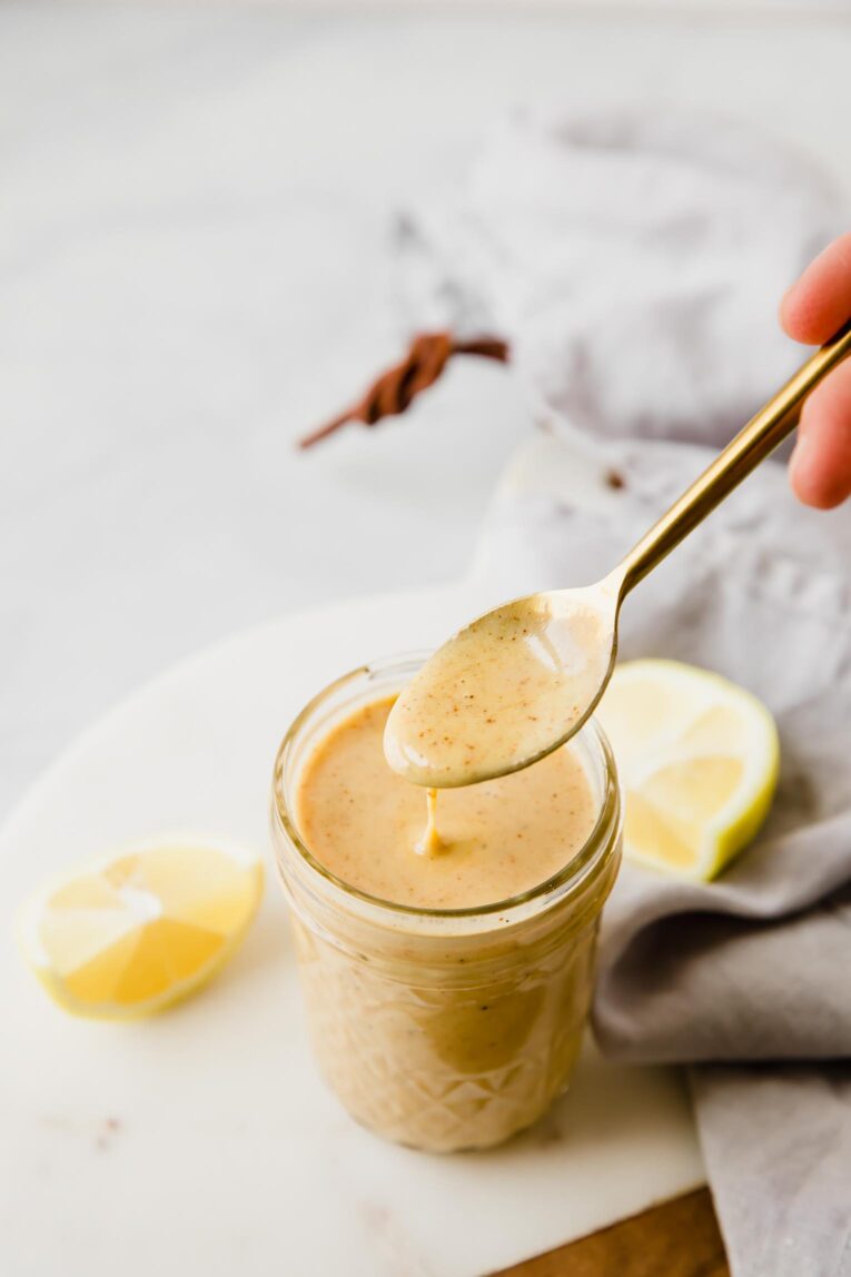 A spoon scooping out honey mustard dressing out of a mason jar.