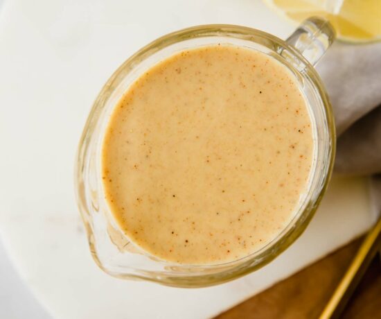 A top shot of a creamer filled with honey mustard on a wooden and ceramic cutting board.