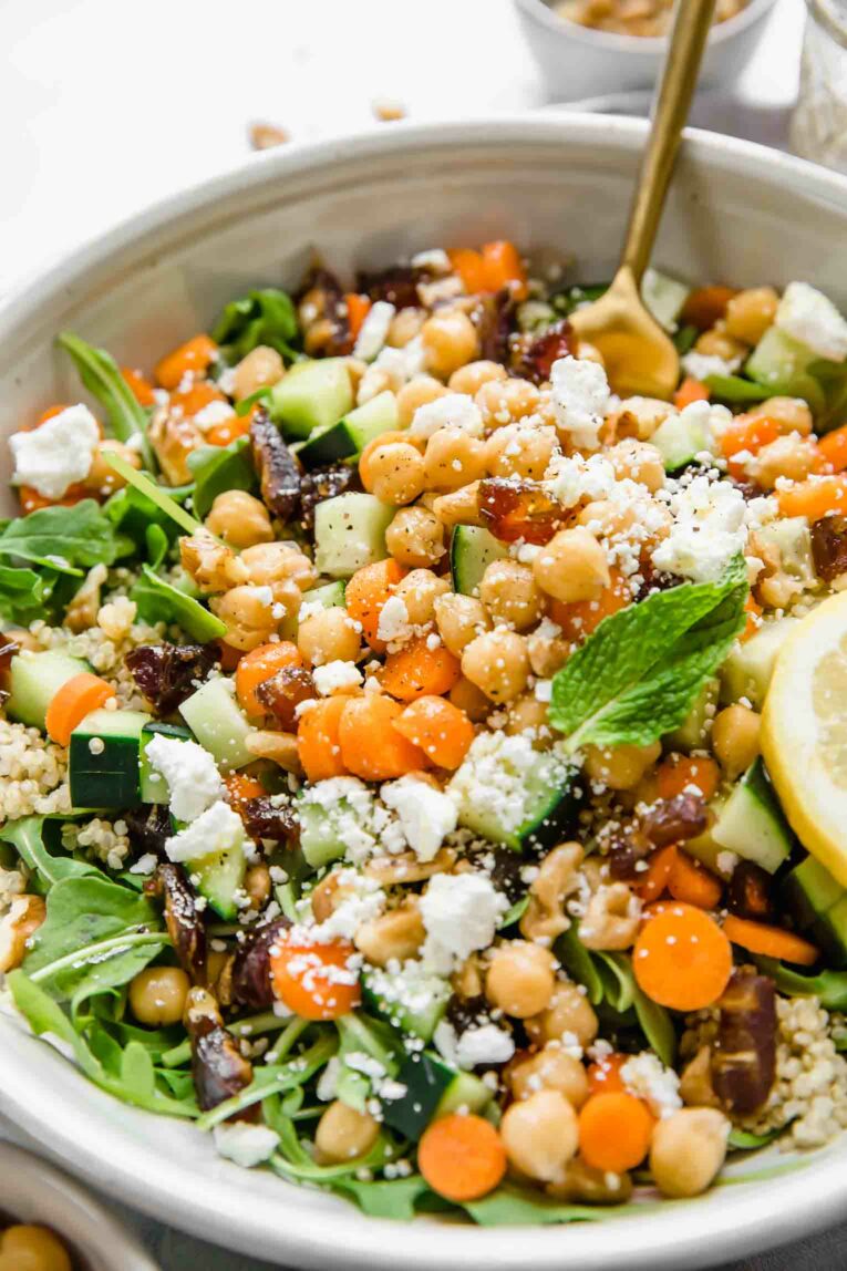 A shot of a large bowl of carrot chickpea salad with feta cheese and a slice of lemon.
