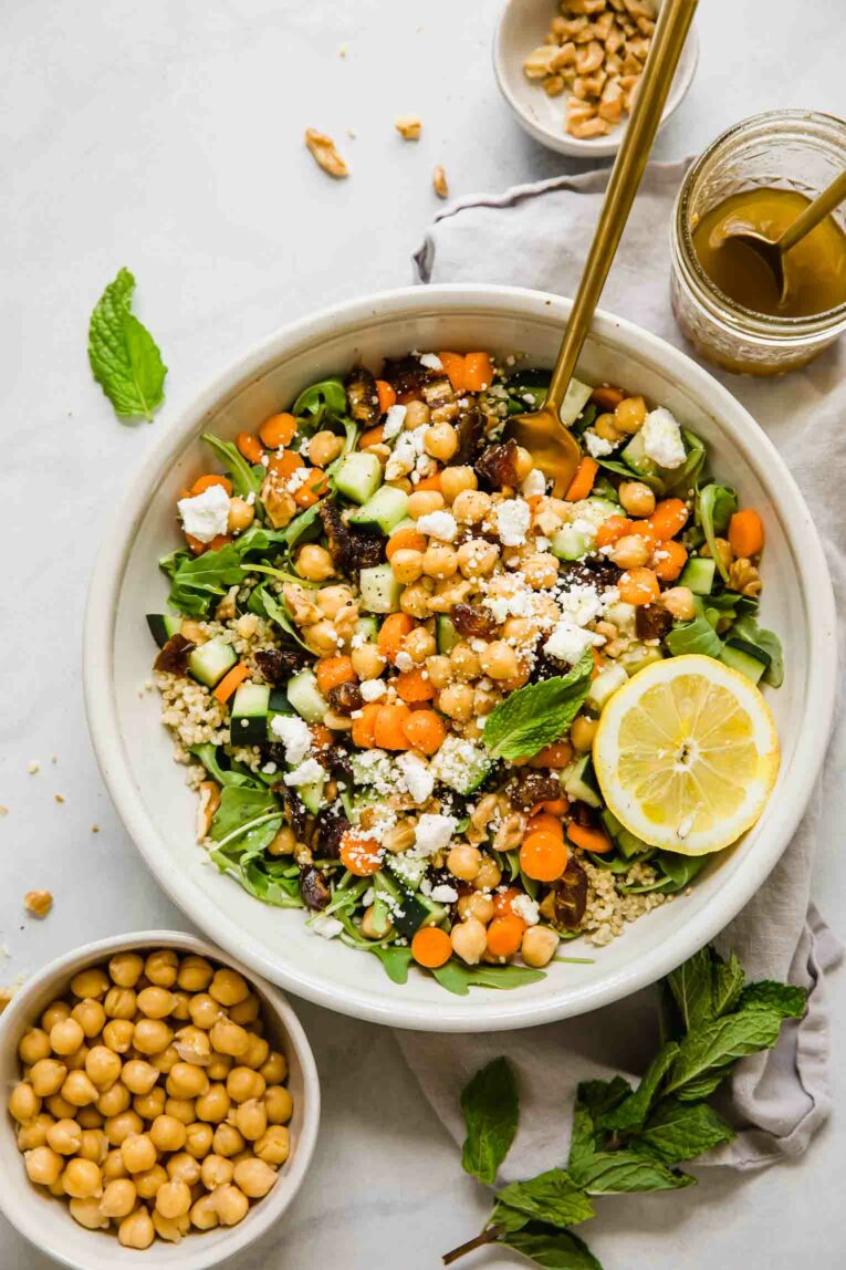 A top shot of a large bowl of carrot chickpea salad with feta cheese and a slice of lemon with a sprig of mint on the side.